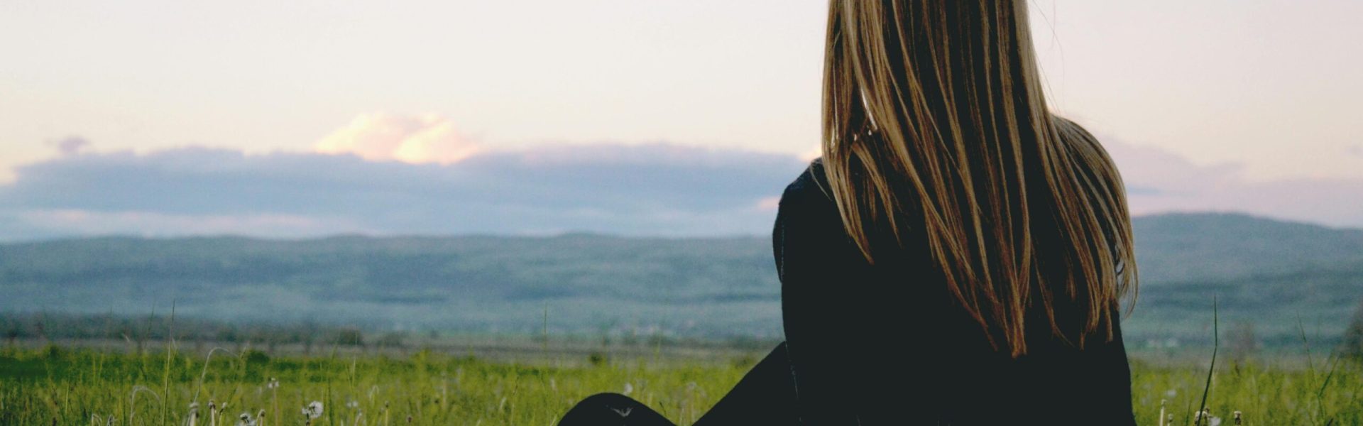 Woman enjoying peace in a lush green field with a scenic mountain view during sunset.